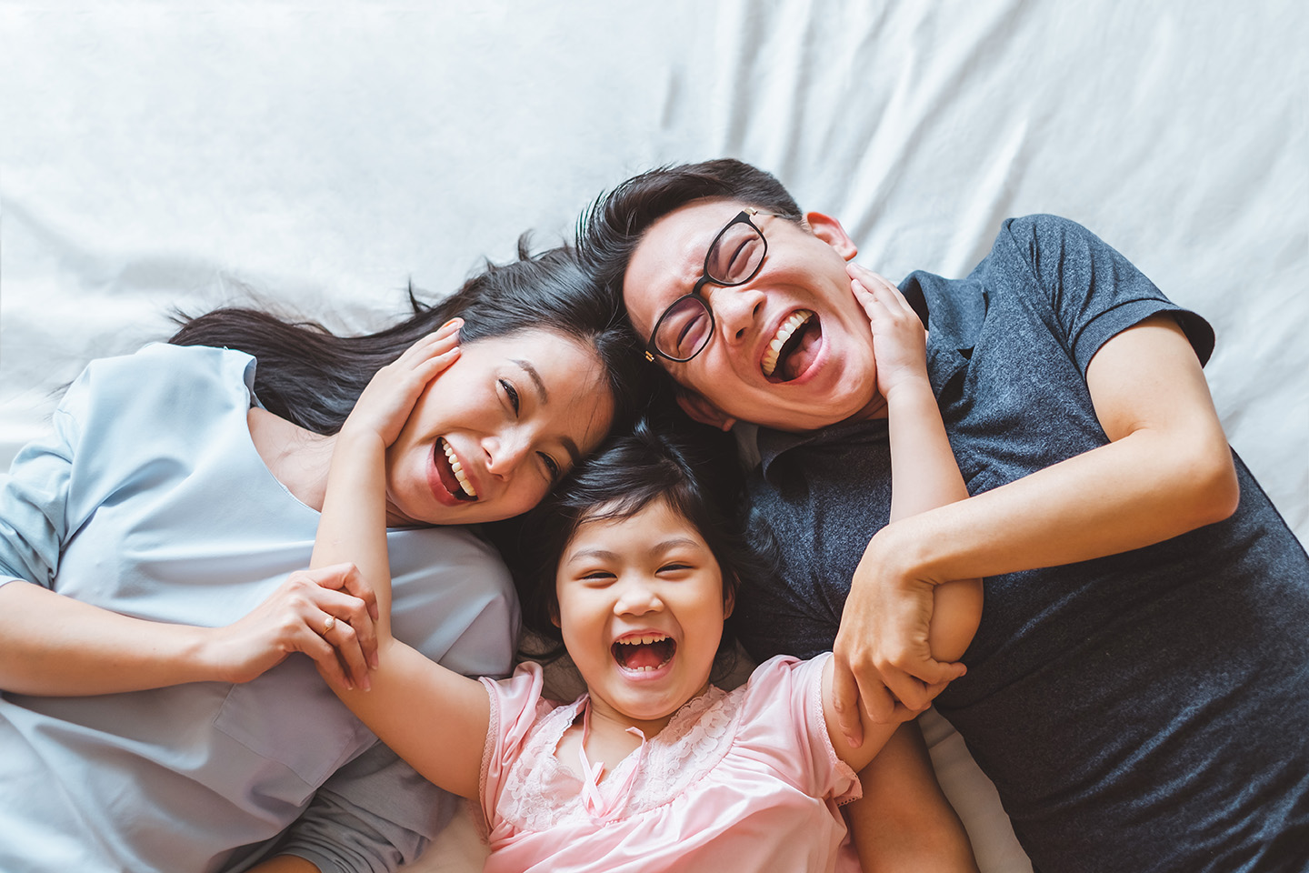 Happy,Asian,Family,Laying,On,Bed,In,Bedroom,With,Happy